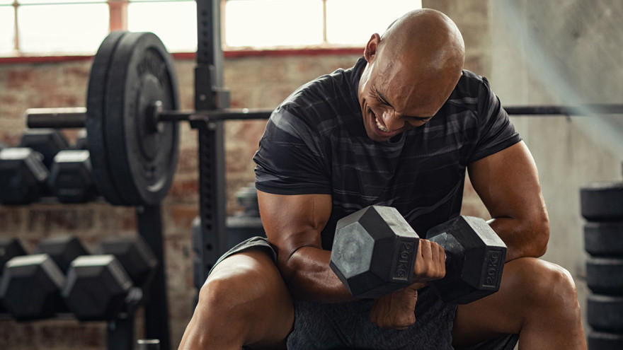 Homme musclé faisant des curls avec haltères en salle de sport.