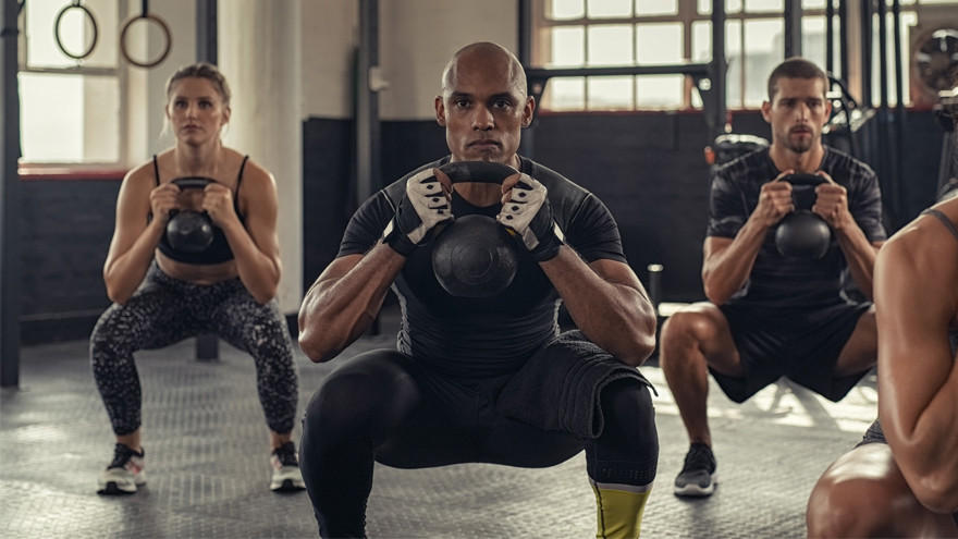 Group performing kettlebell squats in gym with serious expressions.