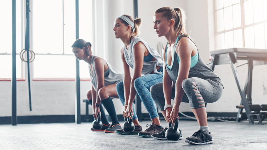 Three women doing kettlebell squats in gym.
