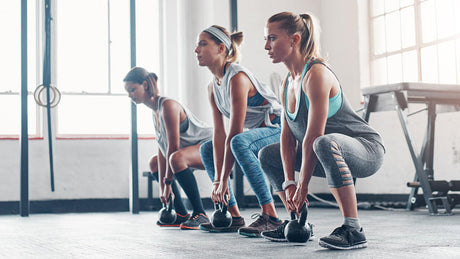 Three women doing kettlebell squats in gym.