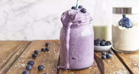 Cremiger Blaubeer-Smoothie läuft aus Glas mit Strohhalm auf Holztisch.