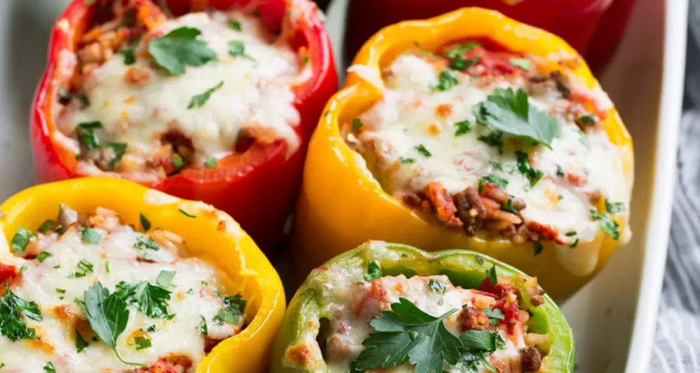 Stuffed bell peppers with cheese, rice, and herbs in white dish.