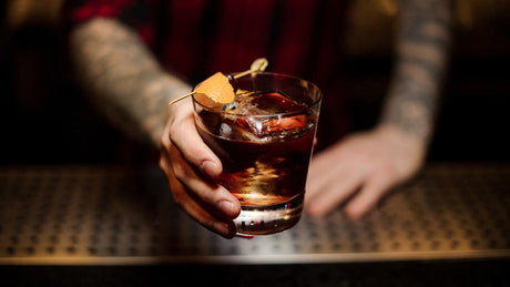 Bartender serving cocktail with ice and orange garnish.