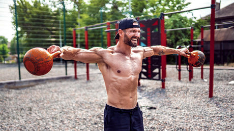 Gespierde man doet schouderoefening met kettlebells buiten.