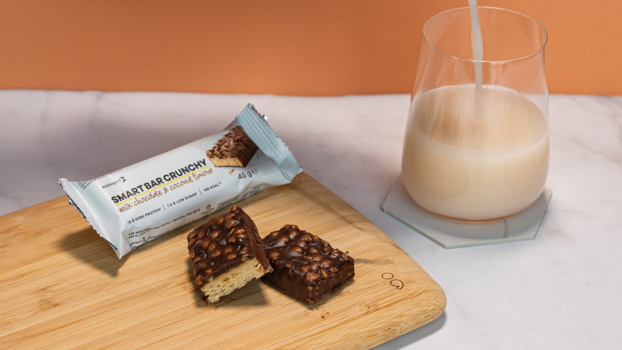 Smart Bar Crunchy protein bar with milk on wooden board.
