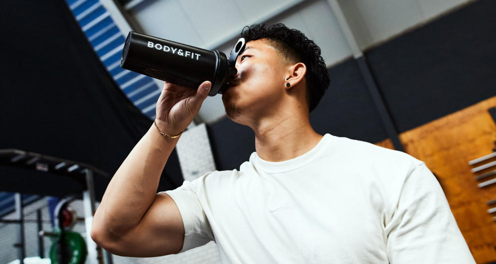 Homme buvant un shaker Body&Fit en salle de musculation.