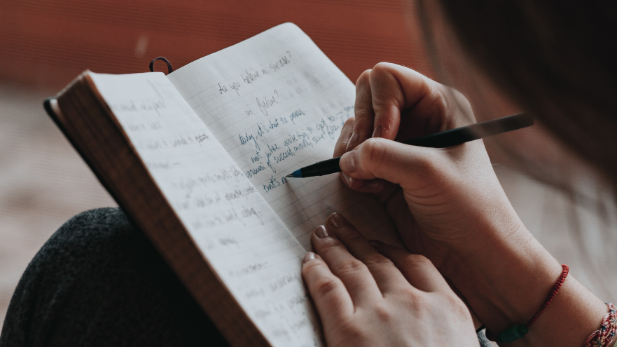 Hand schrijft in notitieboekje met blauwe inkt.