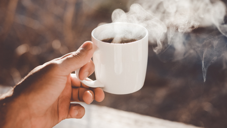 Hand holding steaming cup of black coffee.