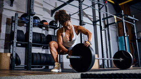 Femme musclée ajustant une barre de musculation en salle.