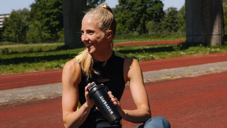 Vrouw met Body&Fit shakebeker op atletiekbaan.