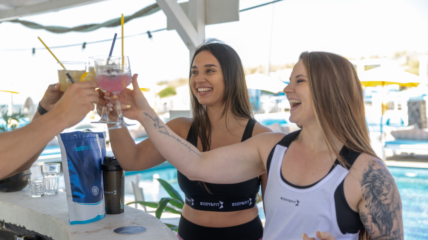 Vrouwen proosten met drankjes bij zwembad in sportkleding.