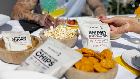 Une sélection de snacks healthy incluant barres protéinées, noix, popcorn et collations chocolatées Body&Fit
