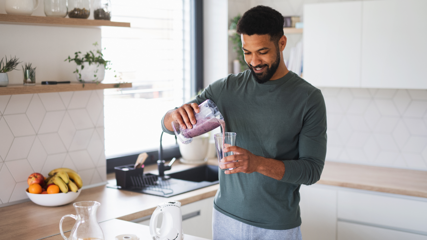 Man schenkt paarse smoothie in glas in moderne keuken.