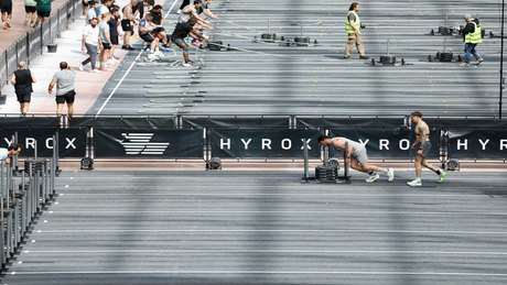 Athletes competing in a HYROX fitness race, performing functional workout exercises in an indoor arena