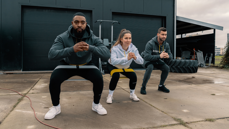 Group doing resistance band squats outside a gym.