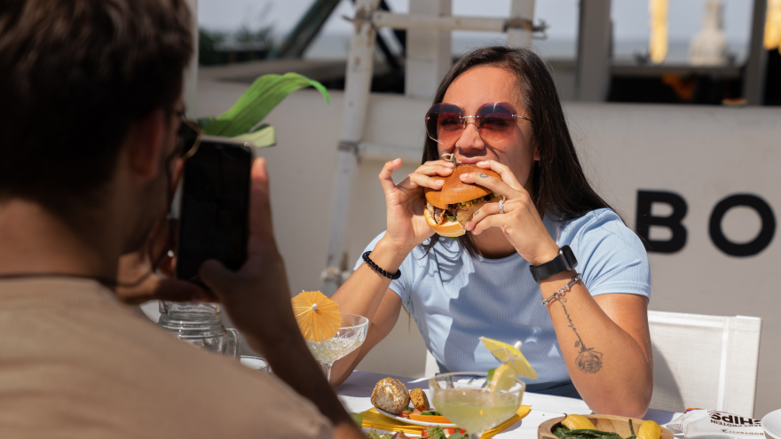 Femme souriante mangeant un burger en terrasse.