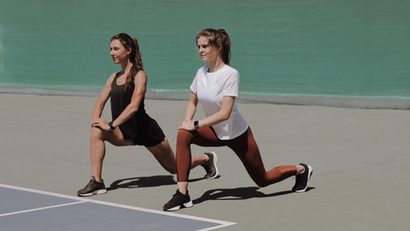 Twee vrouwen doen lunges op tennisbaan.