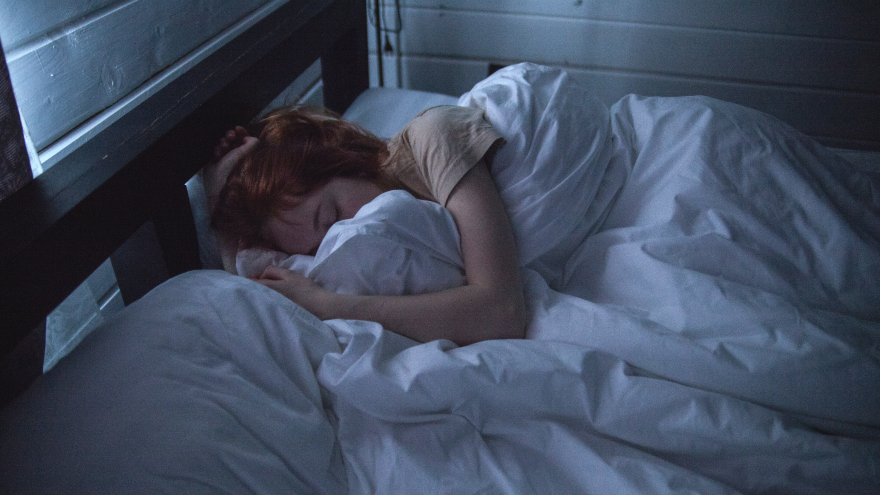 Vrouw slaapt onder wit dekbed in donkere kamer.