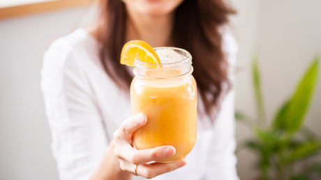 Femme tenant un smoothie orange avec tranche d’orange.