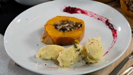 Gefüllter Kürbis mit Kartoffel-Püree und Soßenspur serviert.