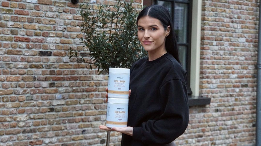 Woman holding Body&Fit collagen protein drink containers outdoors.