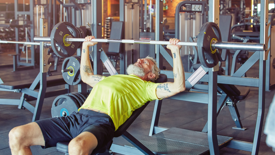 Older man doing bench press at gym.