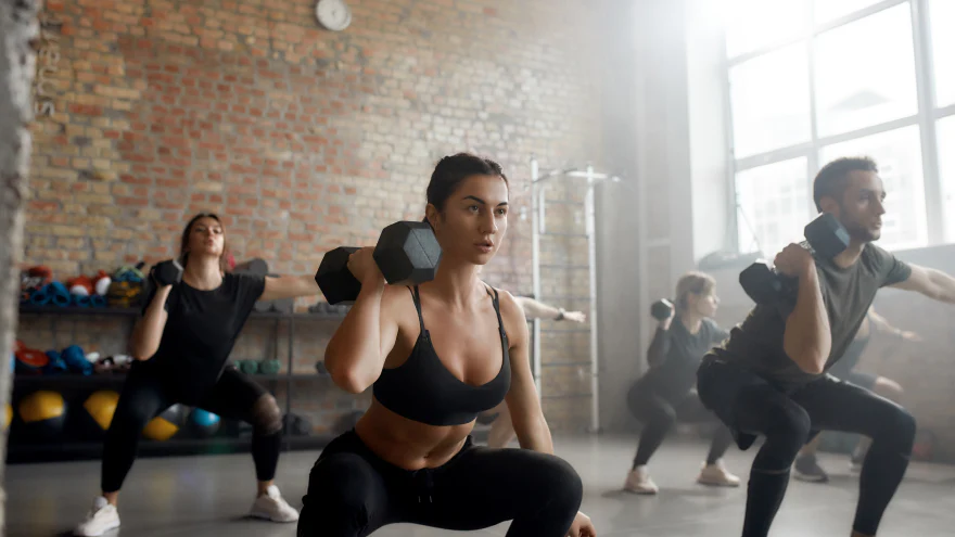 Groupe de fitness réalisant des squats avec des haltères en salle de sport