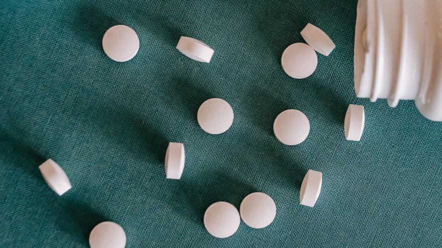 White supplement tablets spilled from bottle on green surface.