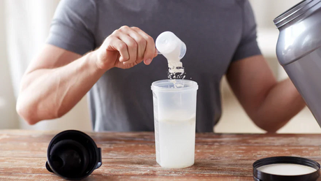 Scooping protein powder into a shaker for post-workout nutrition.