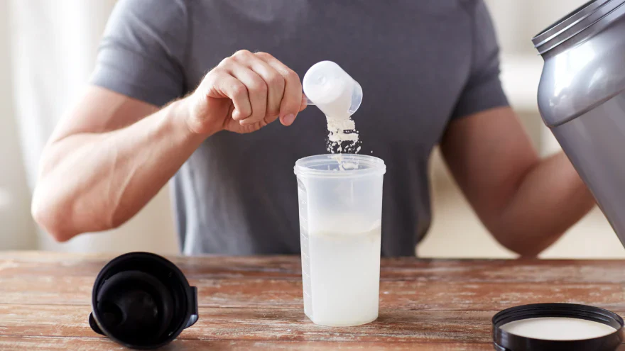 Man schept eiwitpoeder in een shaker voor na de training.