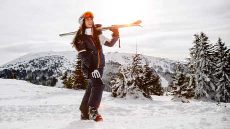 Vrouw draagt ski’s in besneeuwd berglandschap.