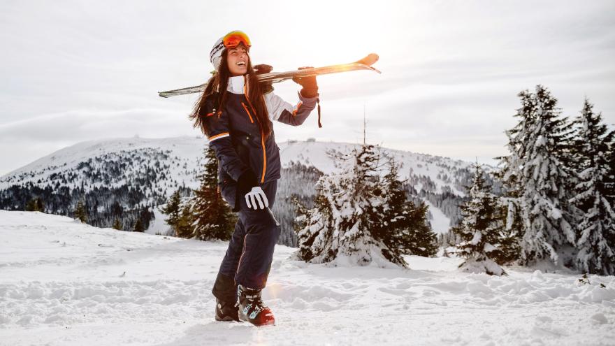 Skieuse souriante portant ses skis en montagne enneigée
.