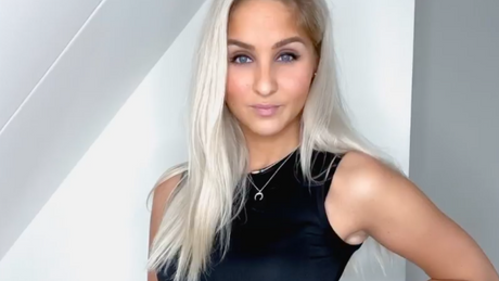 Vrouw poseert in zwarte sporttop met lang blond haar.