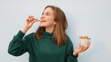 Woman smiling while eating granola from a white bowl.