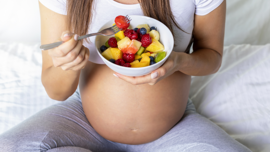 Pregnant woman eating fresh fruit salad in bed.