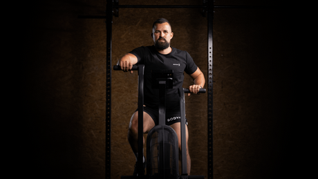 Mann trainiert auf Air Bike im Fitnessstudio mit dunklem Hintergrund.