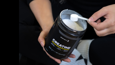 Scooping Body&Fit creatine powder from black container.