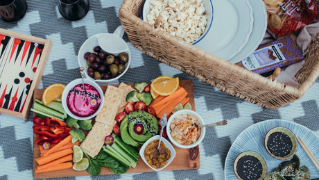 Picknick mit buntem Gemüse, Dips und Snacks auf Decke.