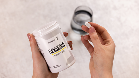 Hand neemt Body&Fit calcium- en magnesiumtablet met glas water.