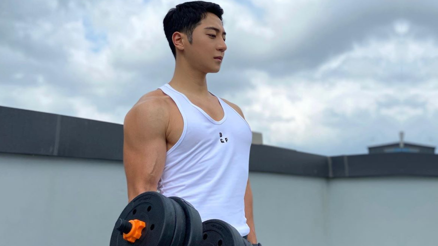 Muscular man doing dumbbell curls on rooftop.
