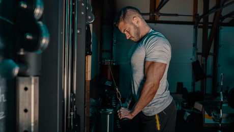 Sportler beim Trizeps-Training an der Kabelmaschine in dunklem Fitnessstudio.