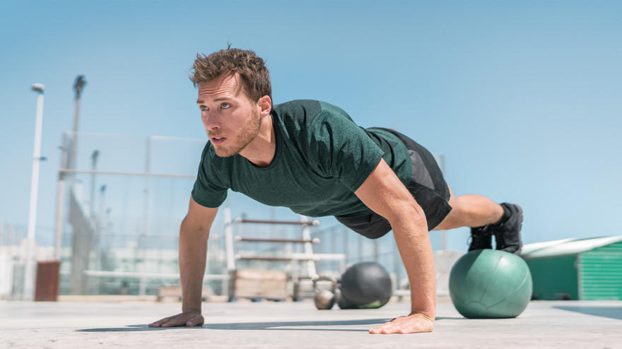 Man doing push-up on medicine ball outdoors.