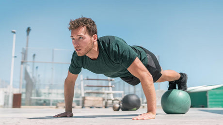 Man doing push-up on medicine ball outdoors.