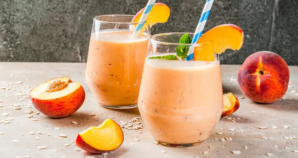 Peach smoothies in glasses with fresh fruit and straws.
