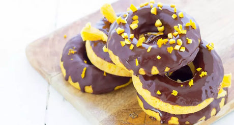Drei Donuts mit Schokoglasur und gelben Streuseln auf Holzplatte.