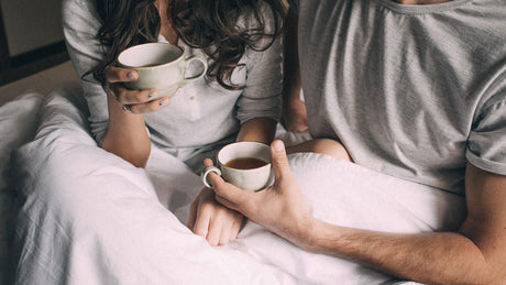 Couple drinking tea together in bed during morning.